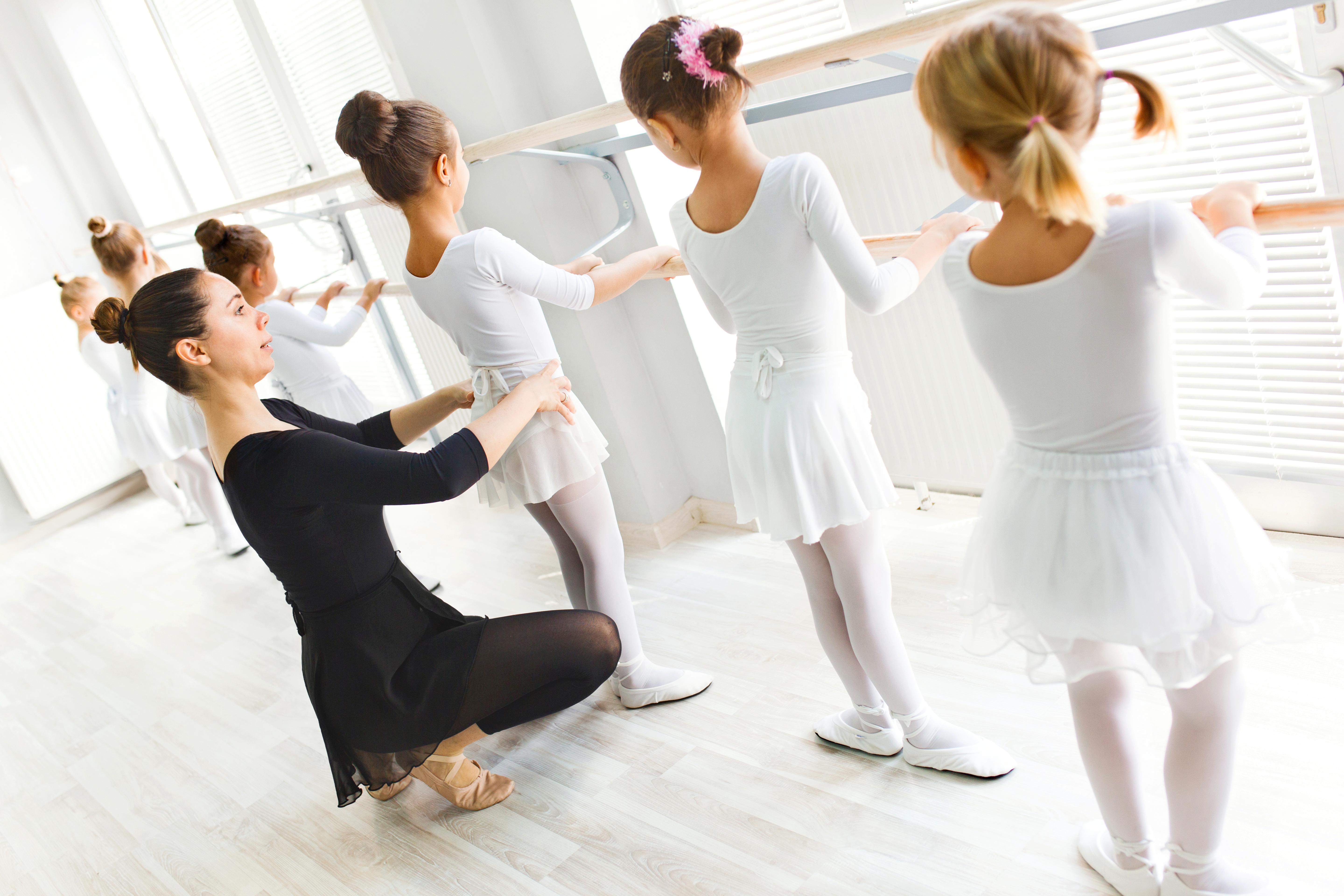Ballet teacher helping girls with postures during ballet class.